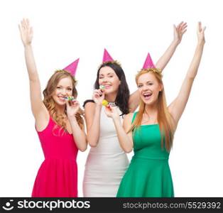 celebration, friends, bachelorette party, birthday concept - three smiling women wearing pink hats and blowing favor horns and waving hands