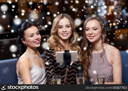 celebration, friends, bachelorette party, technology and christmas holidays concept - happy women with champagne and smartphone selfie stick taking picture at night club over snow
