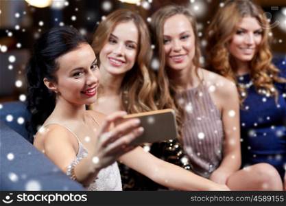 celebration, friends, bachelorette party, technology and christmas holidays concept - happy women with smartphone taking selfie at night club over snow