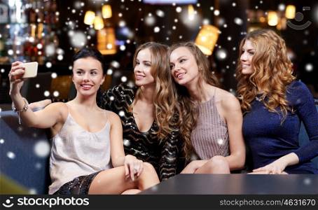 celebration, friends, bachelorette party, technology and christmas holidays concept - happy women with smartphone taking selfie at night club over snow