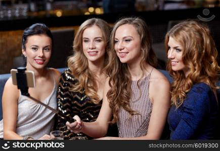 celebration, friends, bachelorette party, technology and holidays concept - happy women with smartphone selfie stick taking picture at night club