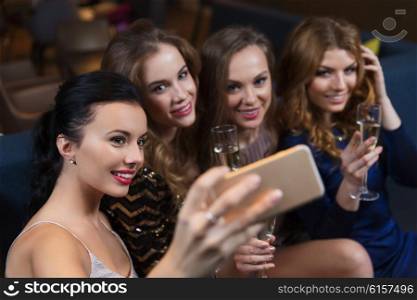 celebration, friends, bachelorette party, technology and holidays concept - happy women with champagne glasses and smartphone taking selfie at night club