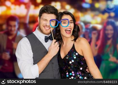 celebration, fun and holidays concept - happy couple posing with party glasses over night club lights background. happy couple with party glasses having fun