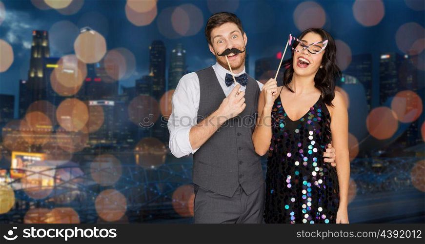 celebration, fun and holidays concept - happy couple posing with party props over singapore city night lights background. happy couple with party props having fun. happy couple with party props having fun