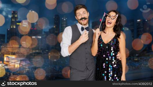 celebration, fun and holidays concept - happy couple posing with party props over singapore city night lights background. happy couple with party props having fun. happy couple with party props having fun