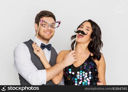 celebration, fun and holidays concept - happy couple posing with party props. happy couple with party props having fun