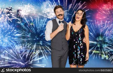 celebration, fun and holidays concept - happy couple posing with party props over firework background. happy couple with party props having fun