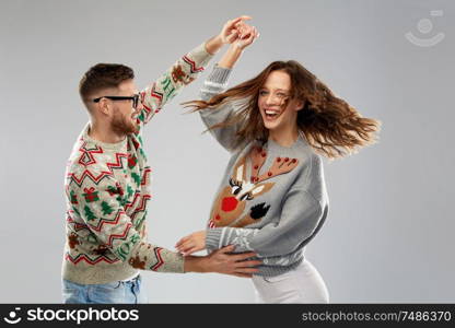 celebration, fun and holidays concept - happy couple wearing ugly sweaters dancing at christmas party. couple dancing at christmas ugly sweaters party