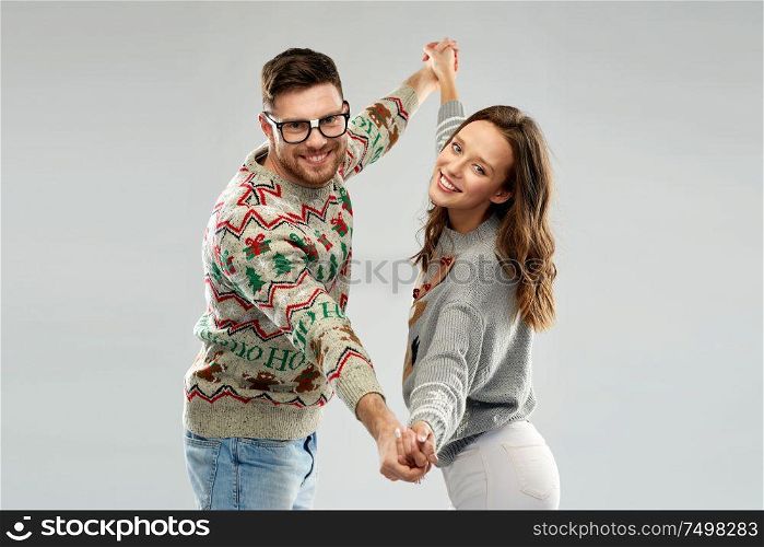 celebration, fun and holidays concept - happy couple wearing ugly sweaters dancing at christmas party. couple dancing at christmas ugly sweaters party