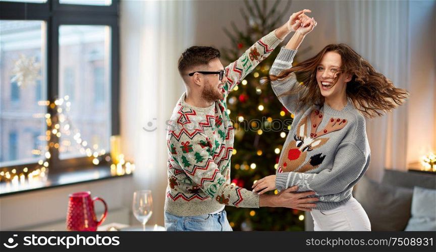 celebration, fun and holidays concept - happy couple wearing ugly sweaters dancing at christmas party. couple dancing at christmas ugly sweaters party