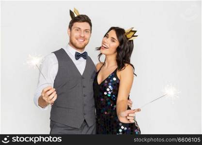 celebration, fun and holidays concept - happy couple with crowns and sparklers at party. happy couple with crowns and sparklers at party