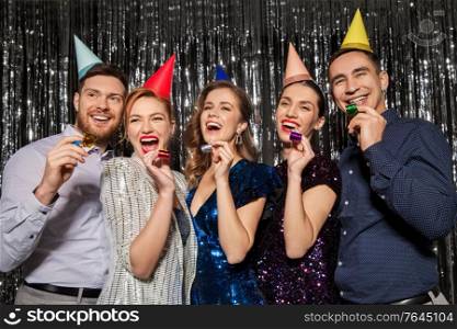 celebration, fun and holidays concept - happy couple with party blowers and birthday caps. happy couple with party blowers having fun