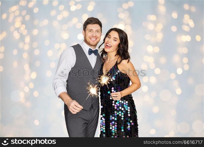 celebration, fun and holidays concept - happy couple with sparklers at party over festive lights background. happy couple with sparklers at party