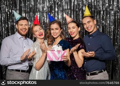 celebration, fun and holidays concept - happy friends in party hats with birthday gift applauding. happy friends in party hats with birthday gift