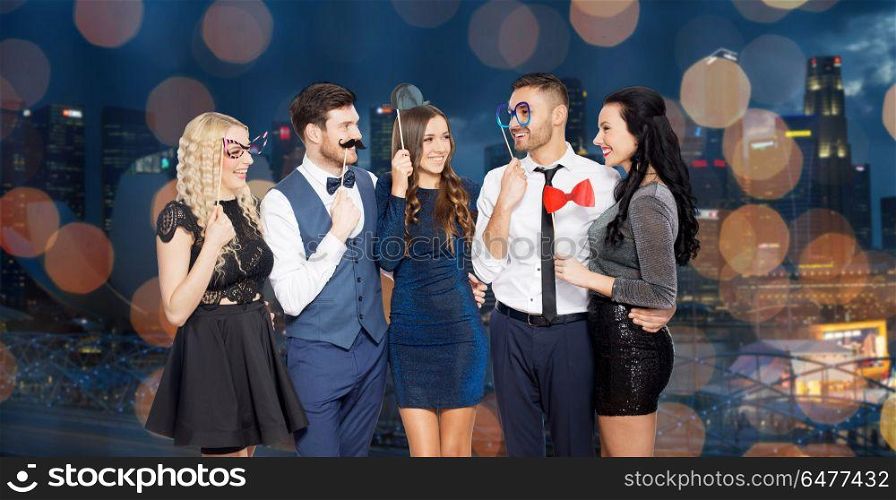 celebration, fun and holidays concept - happy friends posing with party props over night singapore city and lights background. happy friends with party props. happy friends with party props
