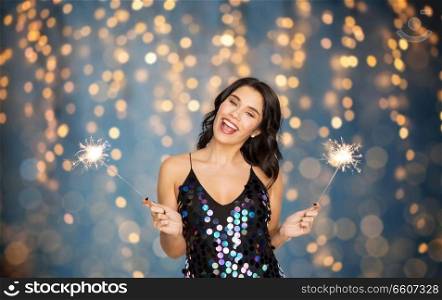 celebration, fun and holidays concept - happy young woman in sequin dress with sparklers at party over festive lights background. happy young woman with sparklers at party