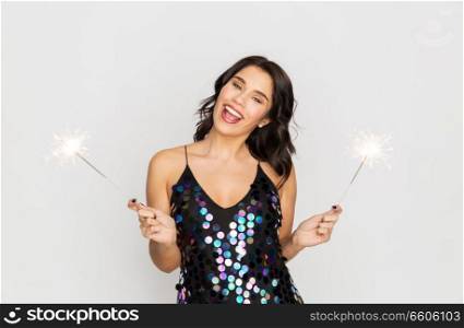 celebration, fun and holidays concept - happy young woman in sequin dress with sparklers at party. happy young woman with sparklers at party