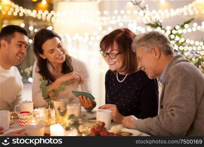 celebration, holidays and people concept - happy family with smartphone having tea party at home. happy family with smartphone at tea party at home