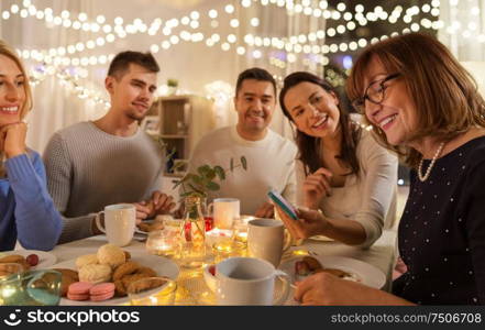 celebration, holidays and people concept - happy family with smartphone having tea party at home. happy family with smartphone at tea party at home