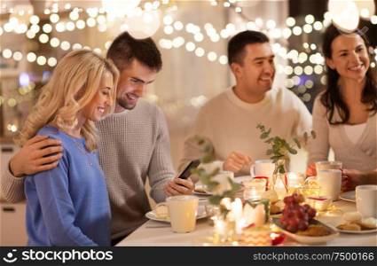 celebration, holidays and people concept - happy friends or family with smartphone having tea party at home. happy friends with smartphone at tea party at home
