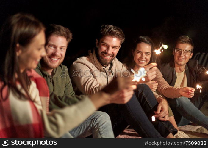 celebration, holidays and people concept - happy friends with sparklers on beach at night. happy friends with sparklers on beach at night