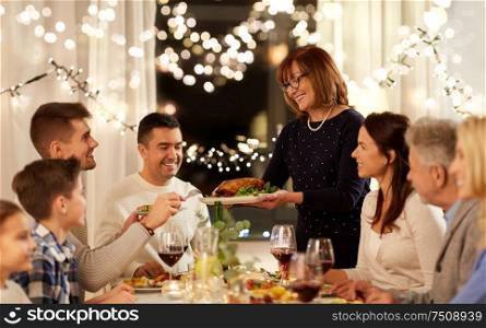 celebration, holidays and people concept - happy senior woman offering roast chicken to family having dinner party at home. happy family having dinner party at home