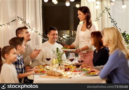 celebration, holidays and people concept - happy woman offering roast chicken to family having dinner party at home. happy family having dinner party at home