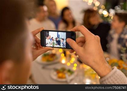celebration, holidays and people concept - man with smartphone taking picture of family at dinner party. man taking picture of family at dinner party