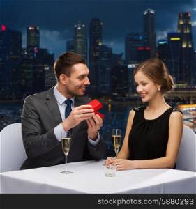 celebration, , holidays and people concept - smiling couple with red gift box at restaurant over night city background