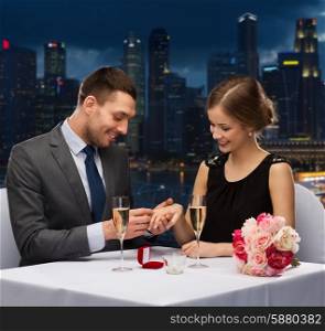 celebration, holidays and people concept - smiling couple with red gift box and wedding ring at restaurant over night city background