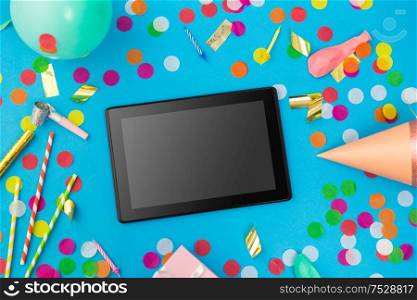 celebration, holidays and technology concept - black tablet computer, birthday party props and colorful confetti on blue background. tablet computer, birthday gift and party props