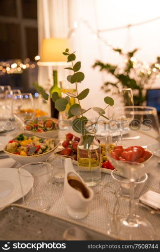 celebration, holidays, catering and eating concept - eucalyptus branch on table served with plates, wine glasses and food for home dinner party. table served with plates, wine glasses and food