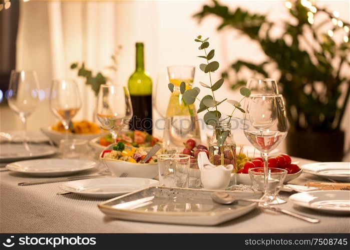 celebration, holidays, catering and eating concept - eucalyptus branch on table served with plates, wine glasses and food for home dinner party. table served with plates, wine glasses and food