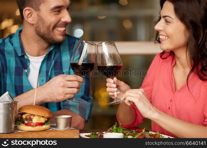 celebration, leisure and holidays concept - happy young couple eating and clinking glasses of red wine at restaurant. couple eating and drinking red wine at restaurant