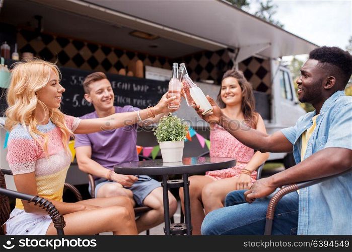 celebration, leisure and people concept - happy friends clinking bottles with drinks at food truck. friends clinking bottles with drinks at food truck