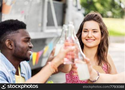 celebration, leisure and people concept - happy friends clinking bottles with non alcoholic drinks at food truck. friends clinking bottles with drinks at food truck