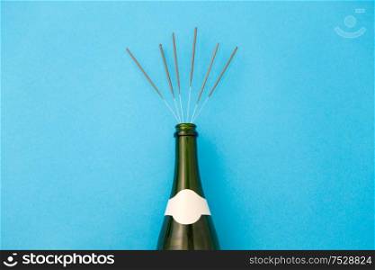 celebration, party and holidays concept - champagne bottle with sparklers on blue background. champagne bottle with sparklers on blue