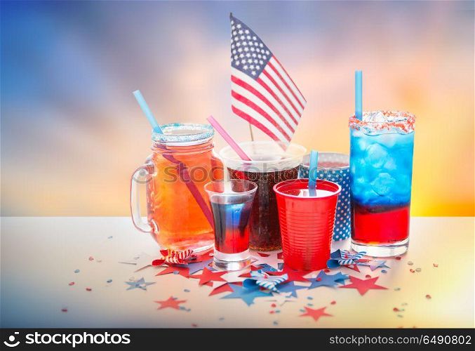 celebration, patriotism and holidays concept - close up of drinks in cups and glasses with american flag at independence day party over evening sky background. drinks on american independence day party. drinks on american independence day party