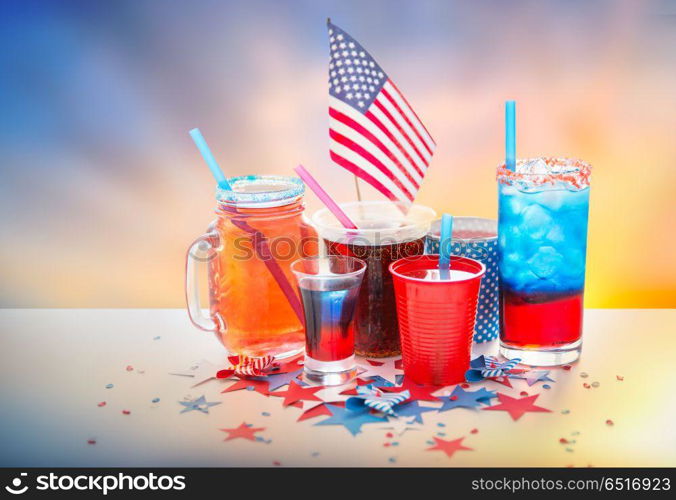 celebration, patriotism and holidays concept - close up of drinks in cups and glasses with american flag at independence day party over evening sky background. drinks on american independence day party. drinks on american independence day party