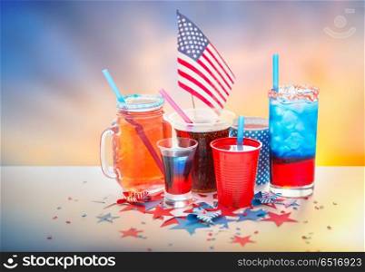 celebration, patriotism and holidays concept - close up of drinks in cups and glasses with american flag at independence day party over evening sky background. drinks on american independence day party. drinks on american independence day party