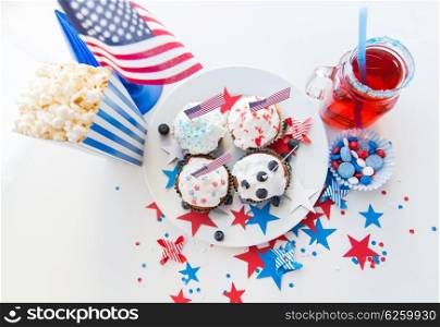 celebration, patriotism and holidays concept - close up of glazed cupcakes decorated with american flags, juice glass or mason jar, popcorn and candies at 4th july party on independence day