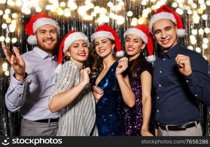 celebration, people and holiday concept - happy friends in santa hats at christmas party over foil fringe and garland lights on background. happy friends in santa hats at christmas party