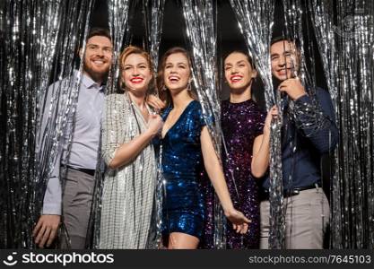 celebration, people and holiday style concept - happy friends in party clothes with tinsel fringe curtain over black background. happy friends in party clothes with tinsel curtain