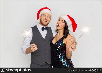 celebration, people and holidays concept - happy couple in santa hats at christmas or new year party with sparklers. happy couple in santa hats at christmas party