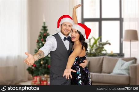 celebration, people and holidays concept - happy couple in santa hats at new year party over christmas tree on home background. happy couple in santa hats at home on christmas