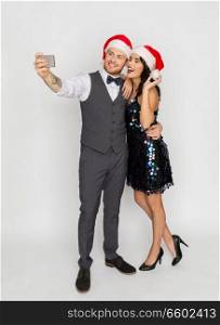 celebration, people and holidays concept - happy couple in santa hats taking selfie by smartphone at christmas or new year party. couple in santa hats aking selfie at christmas