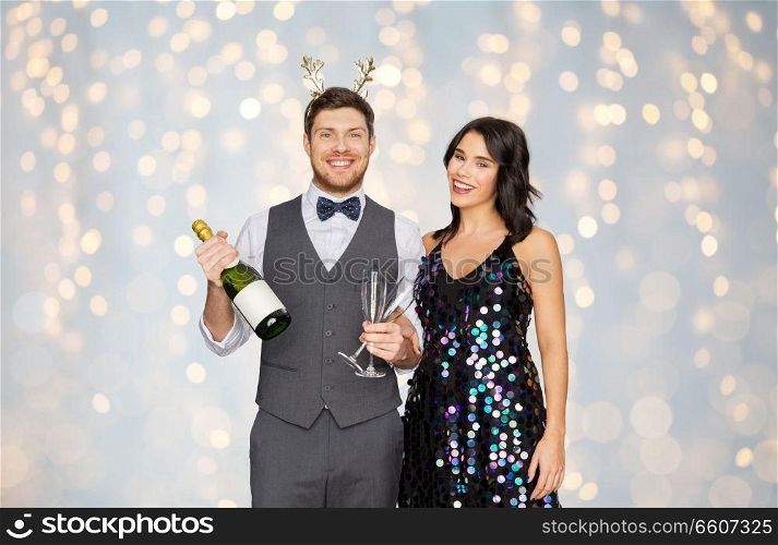 celebration, people and holidays concept - happy couple with bottle of non alcoholic champagne and wine glasses at christmas or new year party over festive lights background. couple with champagne bottle at christmas party