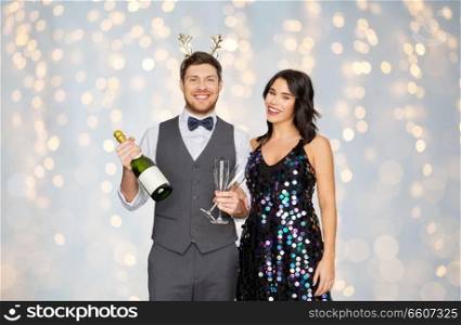celebration, people and holidays concept - happy couple with bottle of non alcoholic champagne and wine glasses at christmas or new year party over festive lights background. couple with champagne bottle at christmas party