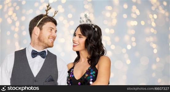celebration, people and holidays concept - happy couple with christmas or new year party props over festive lights background. couple with christmas or new year party props