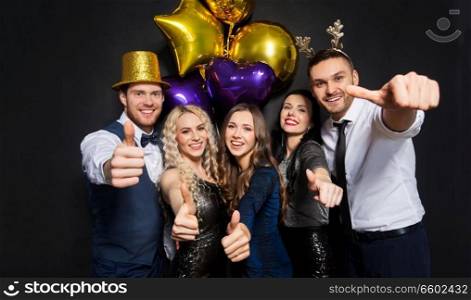 celebration, people and holidays concept - happy friends at christmas or new year party with balloons over black background showing thumbs up. friends at christmas party showing thumbs up